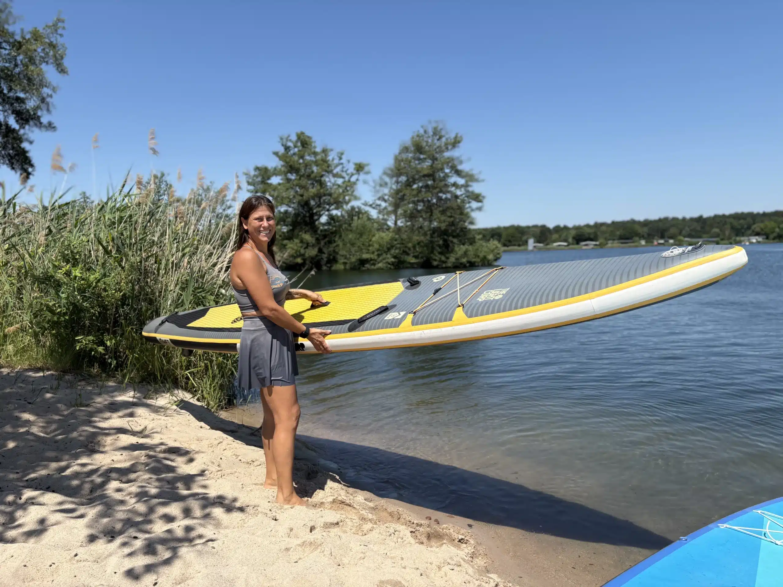 Inhaberin trägt ein SUP-Board am Ufer des Sees in Kahl am See